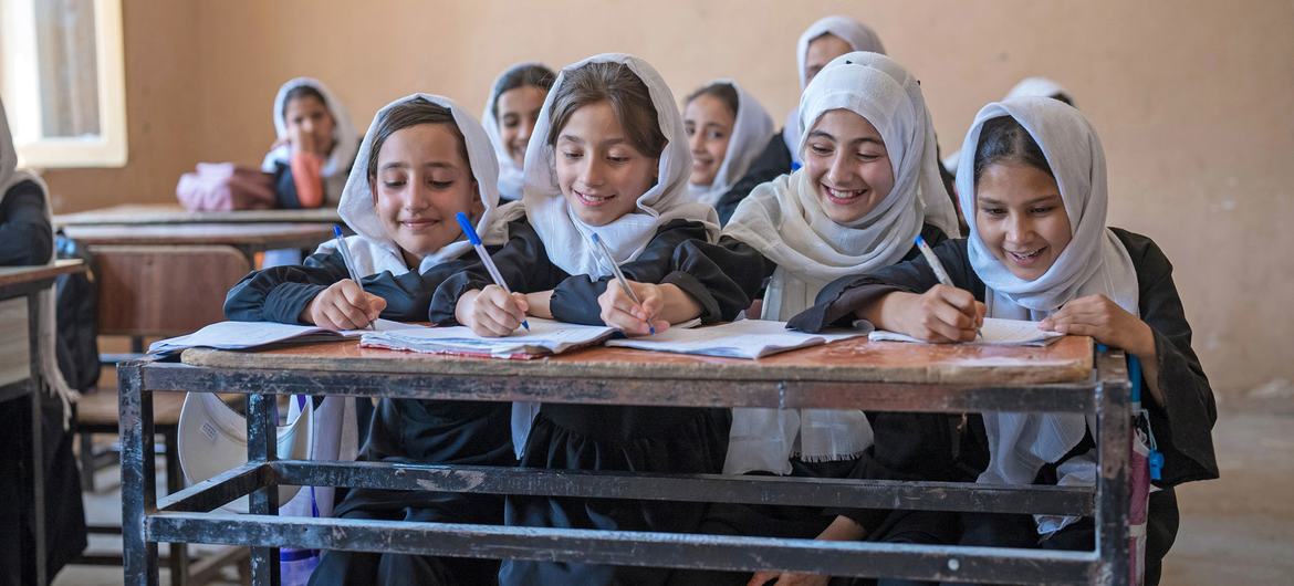 Smiling Afghan schoolgirls writing in their notebooks at their desks