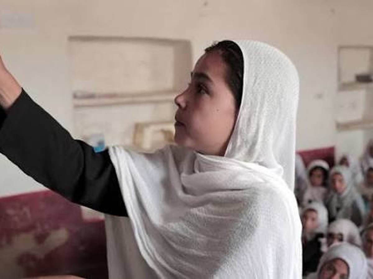 A young teacher writing on the blackboard in front of a class of girls